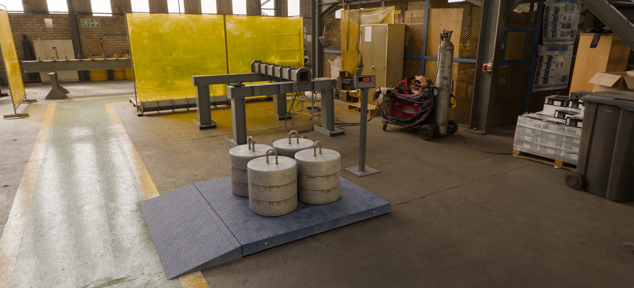 Balança de piso de 2.000 kg calibrada no chão de uma fábrica, com quatro pesos-padrão de 500 kg da Brum sobre a plataforma e o indicador marcando 2000 kg.