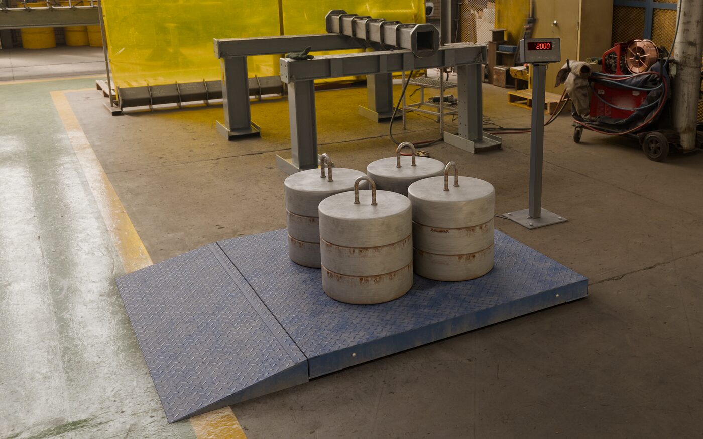 Balança de piso calibrada no chão de uma fábrica, com quatro pesos-padrão de 500 kg da Brum sobre a plataforma e o indicador marcando 2000 kg.