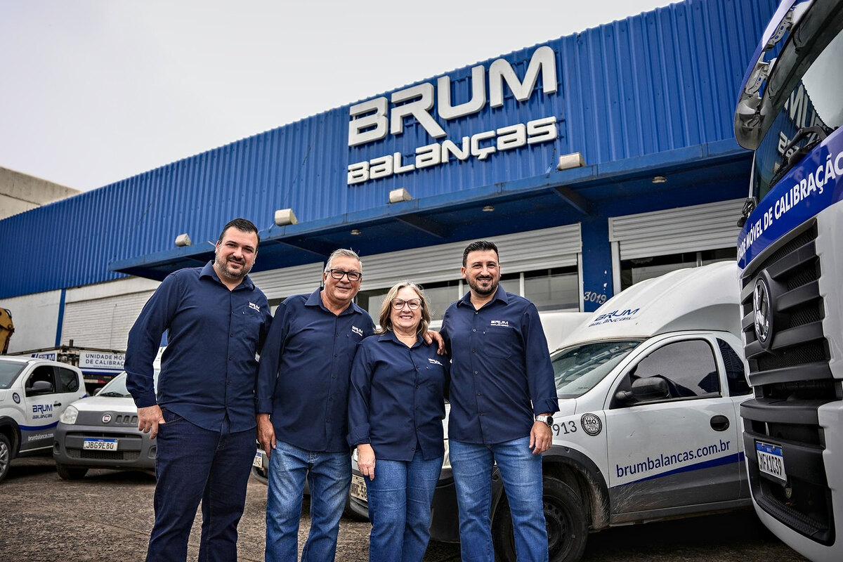 Régis, Darci, Rose e Felipe Brum, de camisa azul-marinho da Brum, em frente à fachada da sede em Canoas, entre um carro de serviço e o caminhão da unidade móvel de calibração.